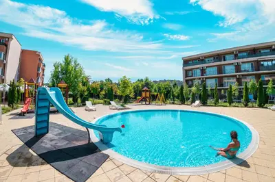 a woman is sitting next to a slide in a pool at Holiday and Orchid Fort Noks Apartments in Sunny Beach