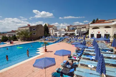 a resort with a swimming pool with blue and white umbrellas at Duni Pelican Hotel - All Inclusive in Sozopol