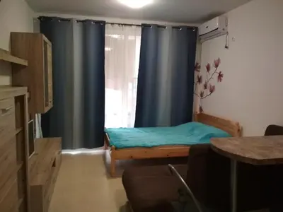 a room with a bed and a window with blue curtains at Виктория in Pomorie