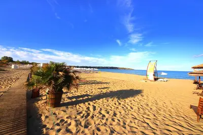a beach with chairs and a sail boat on it at Menada Sozopol Apartments in Sozopol