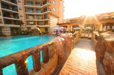 a swimming pool next to a building with the sun shining at Menada Apartments in Karolina in Sunny Beach