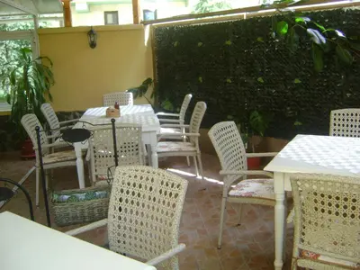 a patio with white tables and chairs and a hedge at Family Hotel Diana in Pomorie