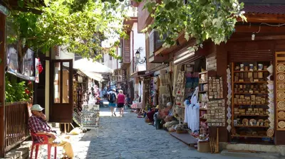 a street with people sitting in chairs in front of shops at Oasis Beach Studios in Sunny Beach