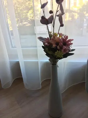 a white vase with flowers in front of a window at Апартамент Мони in Burgas City