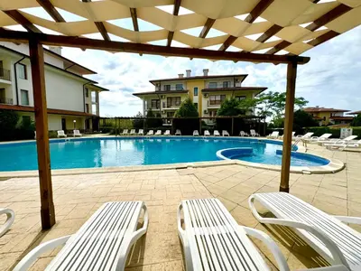 a swimming pool with white chairs and a pergola at Arkite Complex in Sunny Beach