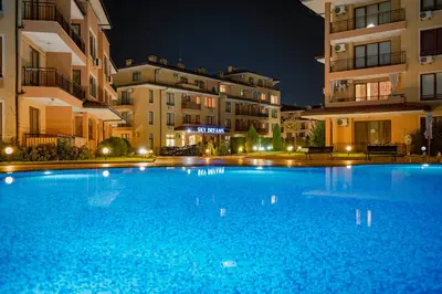 a large blue swimming pool in front of buildings at night at Menada Sky Dreams Apartments in Sveti Vlas