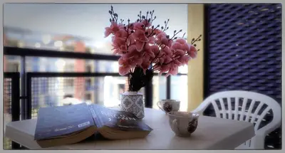a table with a book and a vase with pink flowers at Elit 4 Apartments in Sunny Beach