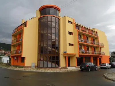 a yellow and orange building with cars parked in a parking lot at Hotel Amigos in Obzor