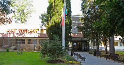 a building with a flag and benches in front of it at Hotel Yunona - All Inclusive in Sunny Beach