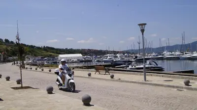 a man riding a scooter down a road near a marina at Sozopoli Hills Simeonov Apartments in Sozopol