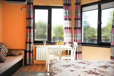 a room with a bed and a table and windows at Къща за гости АКАЦИЯ in Ravna Gora
