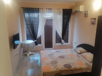 a bedroom with a bed and a table and windows at Къща за гости ЕЛИ in Primorsko