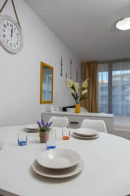 a white table with plates and glasses and a clock at Stylish flat in the TOP centre of Sunny Beach by Flаt Manаger in Sunny Beach