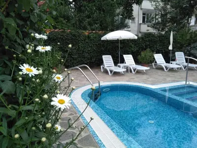 a swimming pool with chairs and an umbrella and flowers at Vila Rosen in Lozenets