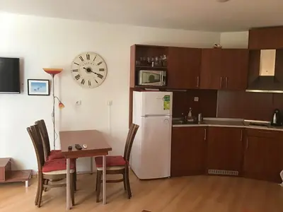 a kitchen with a table and a refrigerator and a clock at SunnySeasons Apartment with swimming pool view in Byala