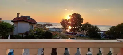 a sunset from a balcony with a house and the ocean at Студио Сънрайз А28, Лозенец in Lozenets
