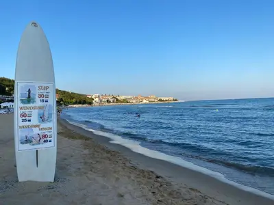 a surfboard sitting on the beach next to the ocean at Sea View Panoramic Apartments, Fort Noks Crown Club in Sveti Vlas