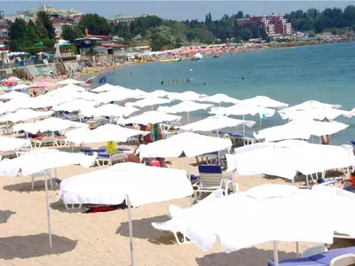a beach with white umbrellas and people in the water at Safo Apartments and Rooms in Sozopol