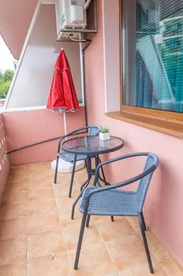 a table and chairs on a balcony with a red umbrella at Къща за гости КАТИ in Kiten