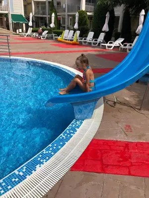 a little girl sitting on a slide next to a swimming pool at ELIT 2 APART HOTEL in Sunny Beach