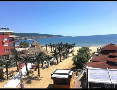 a beach with buildings and palm trees and the ocean at Hotel Largo Beach in Sunny Beach