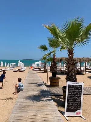 a boardwalk on a beach with palm trees and a sign at Apartment at St. Nicholas Complex-Igora in Chernomorets