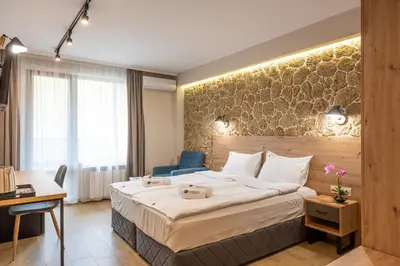 a hotel room with a large bed and a blue chair at Хотел Камъните in Burgas City
