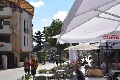 a group of people sitting at a cafe with tables and umbrellas at Top center apartment Gramophone with private parking in Burgas City