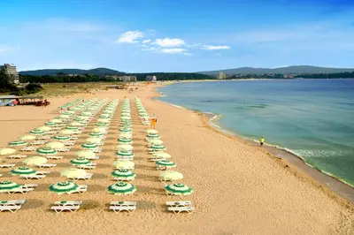 a beach with many lawn chairs and umbrellas at Hotel Forest Beach in Primorsko