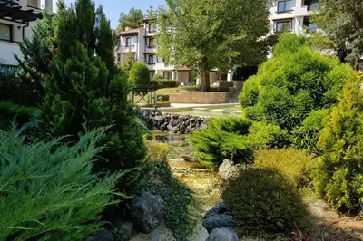 a garden with a creek and trees and a building at Apartment in the picturesque Oasis Resort & Spa in Lozenets