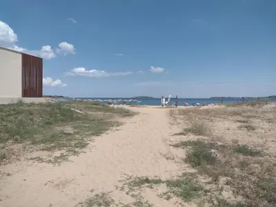 a sandy beach with a building and the ocean at Апартамент на къмпинг Градина in Chernomorets