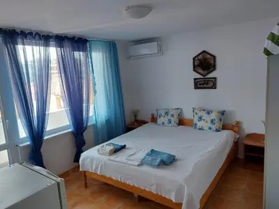 a bedroom with a bed with blue curtains and a window at Стаи за гости WEST in Pomorie