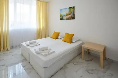 a white bedroom with a bed and a table at Luxury First Line apartment with pool by the sea in Nesebar