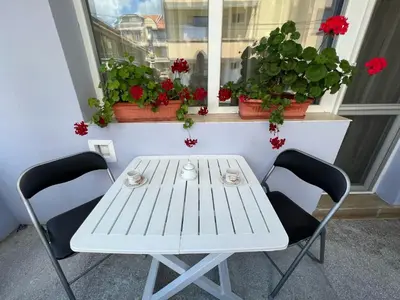 a white table and chairs in front of a window with flowers at Апартамент Иванови in Pomorie