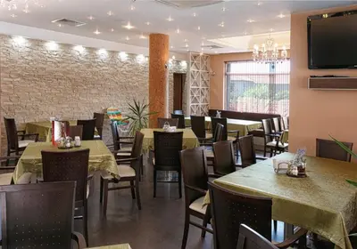 a restaurant with tables and chairs and a flat screen tv at Александра in Sveti Vlas