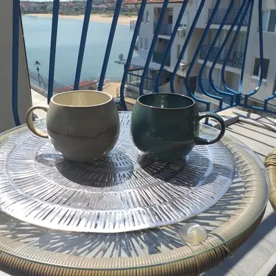 two coffee cups sitting on a glass table on a balcony at Z&Z Apartment in Sozopol