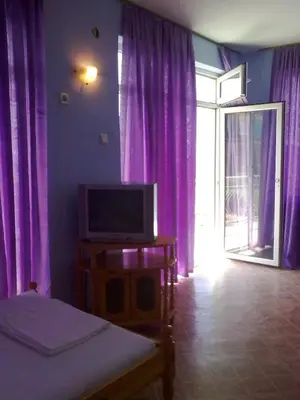 a room with a tv and purple curtains and a window at Вила Синя Иглика in Kosharitsa