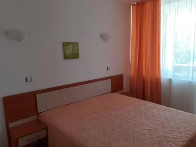 a bedroom with a bed and an orange curtain at Апартамент Полюси 2 in Sunny Beach