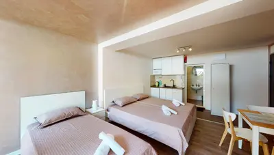 two beds in a room with a table and a kitchen at Markoni 5 in Burgas City