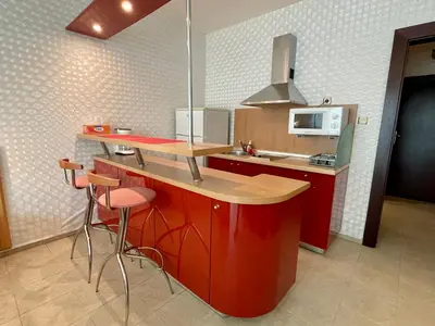 a kitchen with red cabinets and a counter with stools at Sunny Studio in Sunny Beach by Flat Mаnаger in Sunny Beach