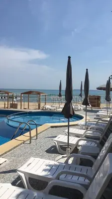 a pool with lounge chairs and umbrellas and the ocean at Апартаменти СЪНИ БЕЙ in Sunny Beach