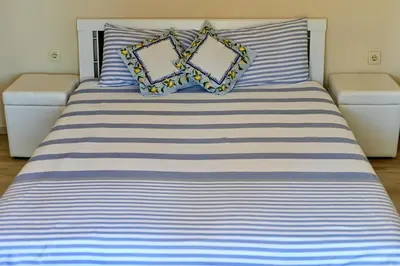 a bed with blue and white striped sheets and pillows at Апартамент Limoncini in Sozopol