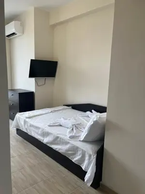 a bedroom with a bed with white sheets and a television at Къща за гости CANAVAN'S in Ravda