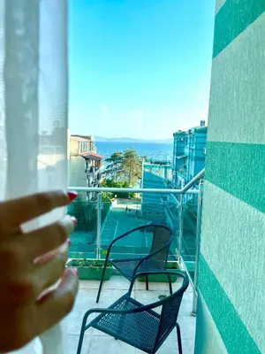 a person looking out a window at a balcony with chairs at Penthouse Panorama Sea View Apt. Pomorie in Pomorie
