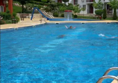 a person swimming in a large blue swimming pool at 2-комнатные апартаменты у моря 10 бассейнов Crown Fort Noks in Sveti Vlas