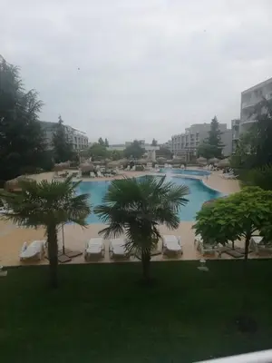 a large swimming pool with chairs and palm trees at Atlantis Resort D111 апартамент in Burgas City