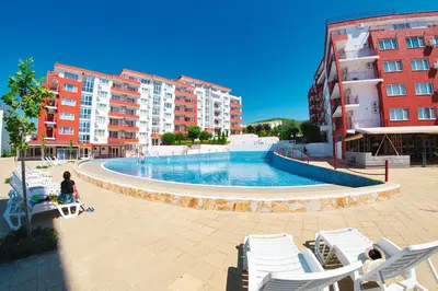 a woman sitting on a bench next to a swimming pool with buildings at Marina View Fort Beach in Sveti Vlas
