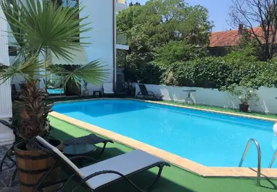 a swimming pool in a resort with chairs and palm trees at Апартамент Холи in Sozopol