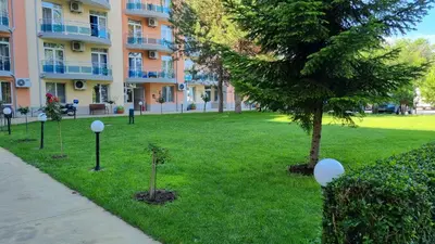 a park in front of a building with a tree at Oasis deluxe apartment by the sea in Ravda