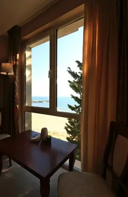 a room with a table and a window with a view of the ocean at Първа линия Апартаменти in Pomorie